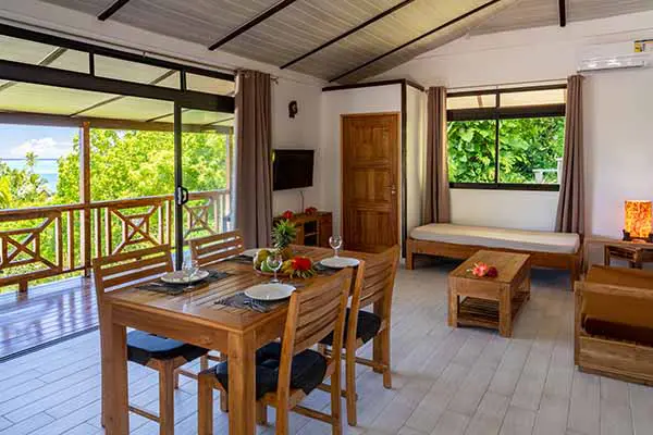 Autre angle de vue de la table à manger avec salon et baie vitrée donnant sur terrasse avec vue sur le lagon dans notre maison de vacances à Bora Bora